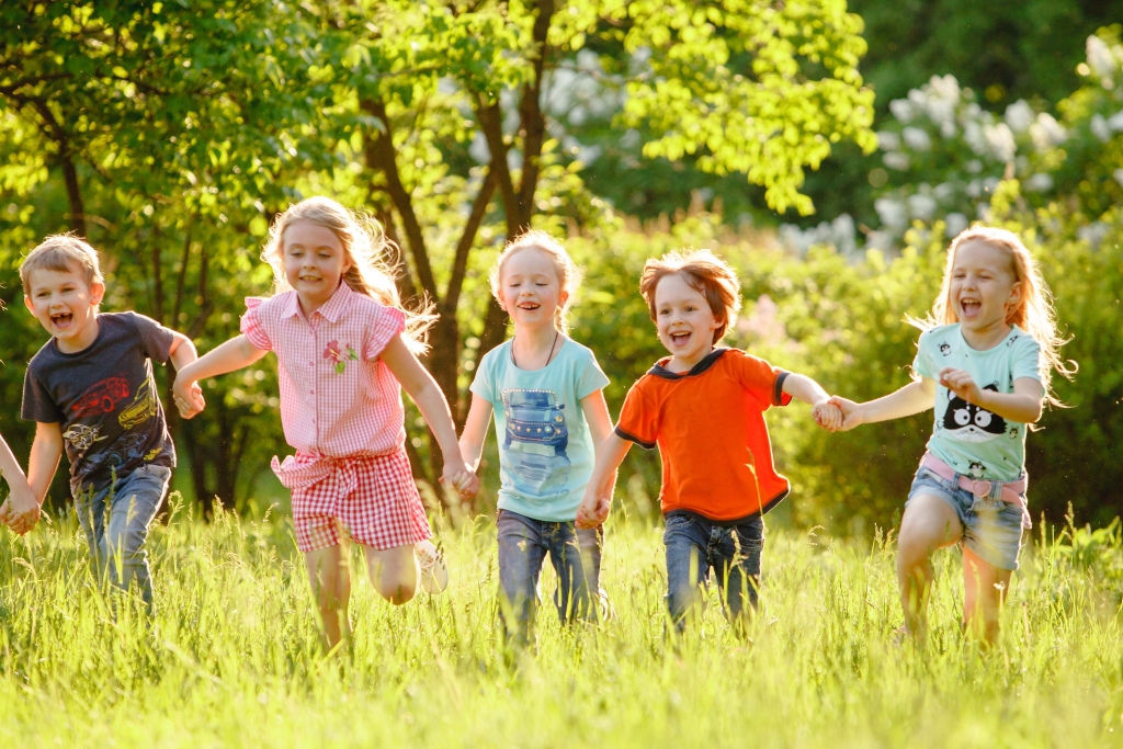 Flere unge barn løper hånd i hånd ute i naturen